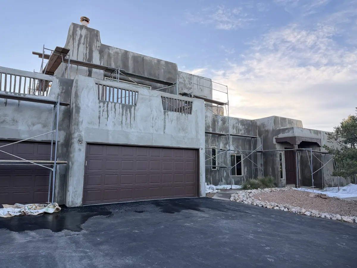 Two story house at the base coat stage with scaffolding across the front and drop cloths on the driveway.