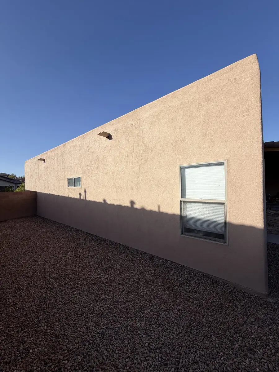 Long blush colored stucco wall running back from a house corner, with canale spouts and a single window.
