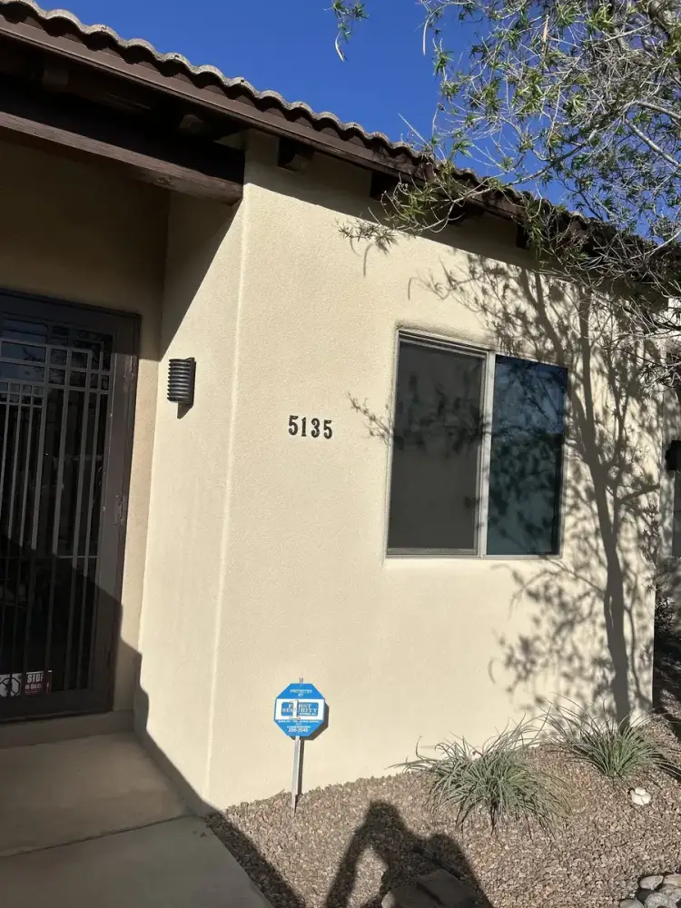 Cream stucco finish around a house entry under a clay tile roof, with the house number on the wall.