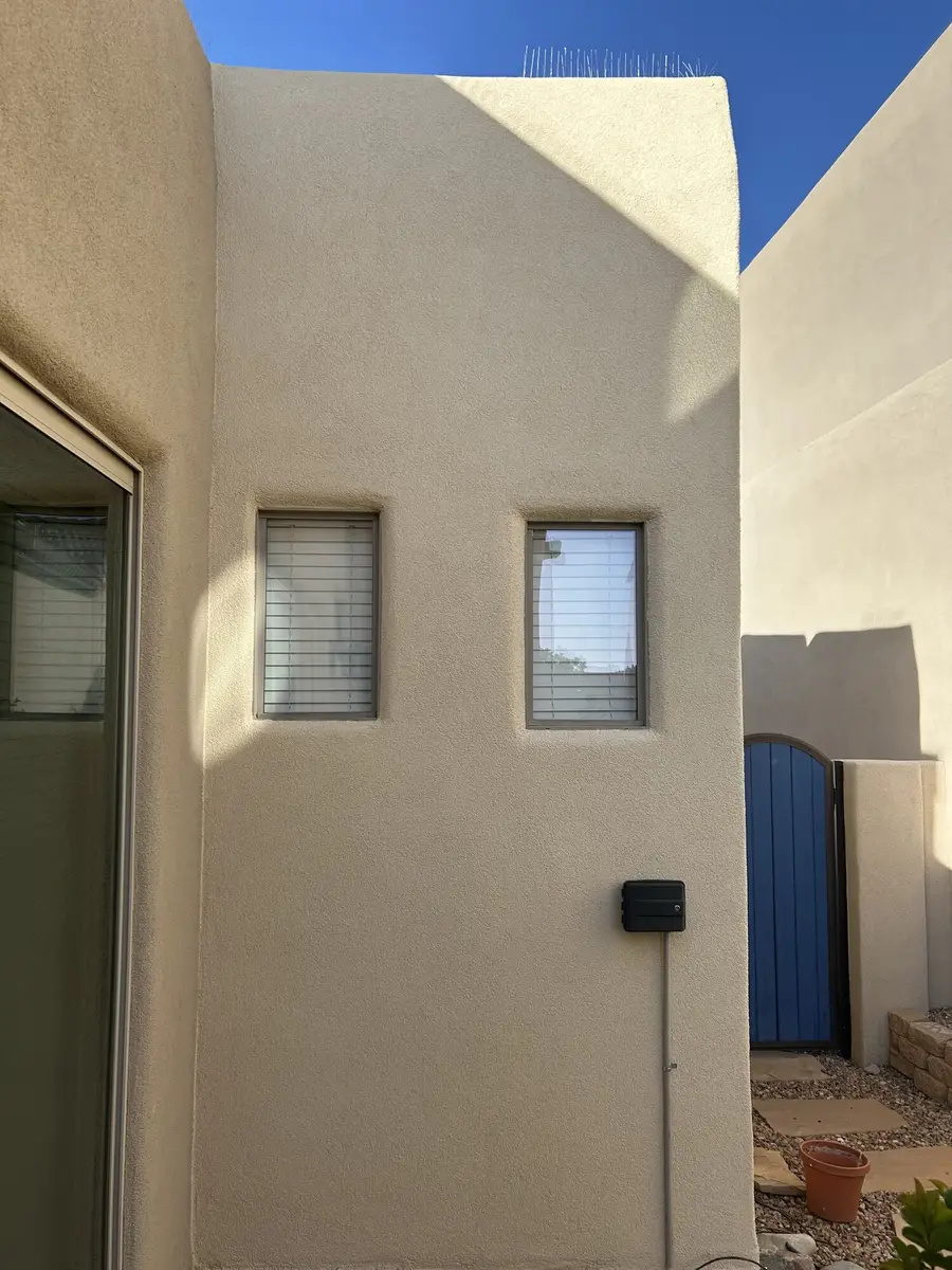 Cream stucco wall on a house side elevation with two small windows and a blue gate beyond.
