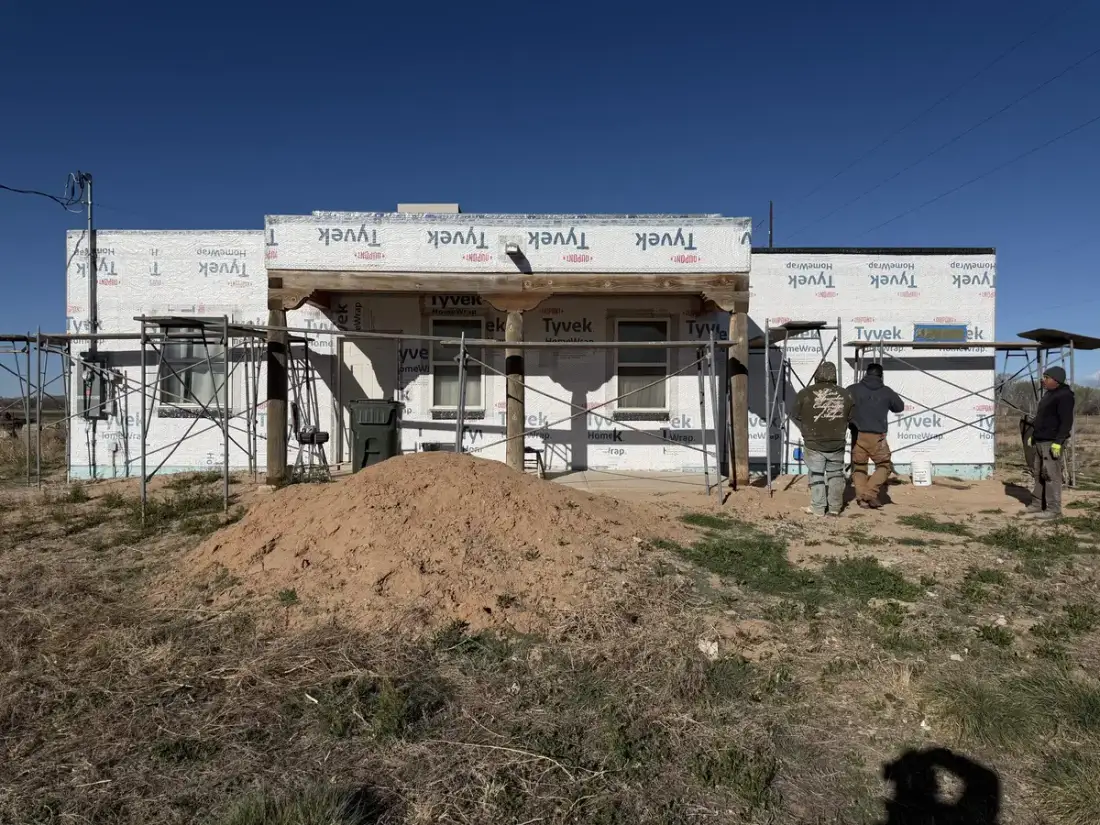 Crew working around a house covered in housewrap with scaffolding set up along the front.