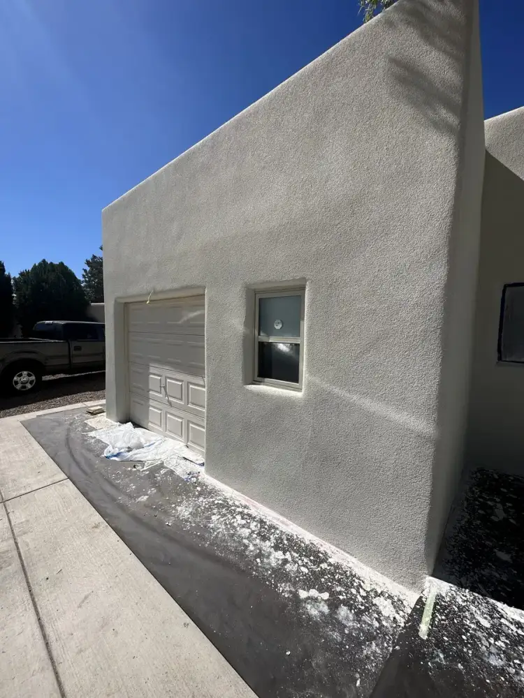Light grey stucco finish on a garage wall, with the drop cloth still down along the driveway.