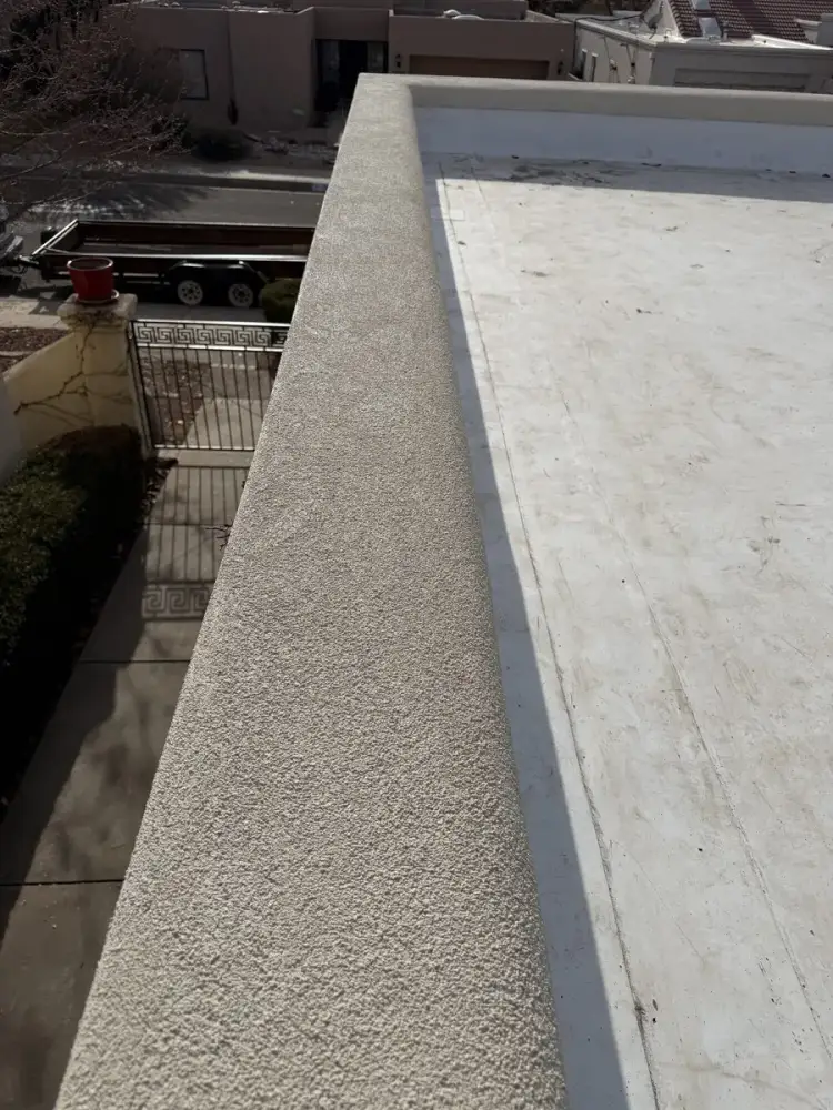 Freshly stuccoed parapet wall running along the edge of a white flat roof.