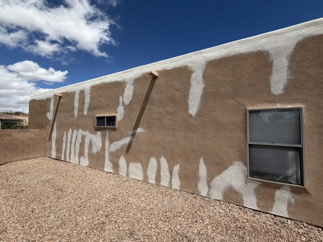Long tan stucco wall covered in white patch repairs where cracks were filled, before the new finish coat.