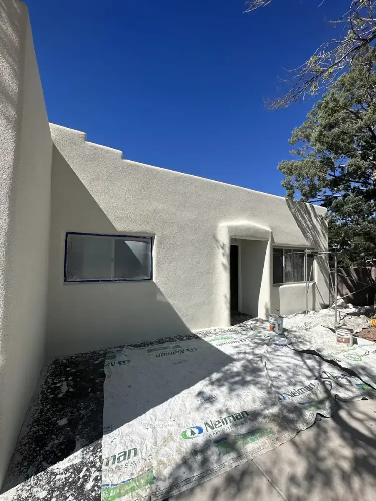Pueblo style house in a pale sage stucco finish with a stepped parapet, windows still masked and drop cloths on the patio.
