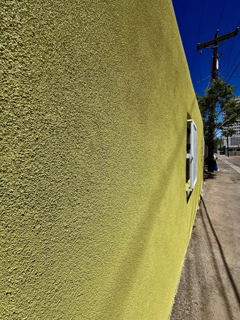 Close view along a yellow green stucco wall showing the heavy sand finish texture.