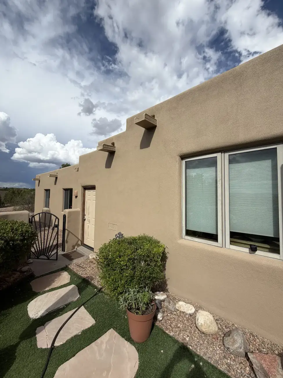 Tan stucco house with stepped parapets and wooden corbels under a sky full of cloud.