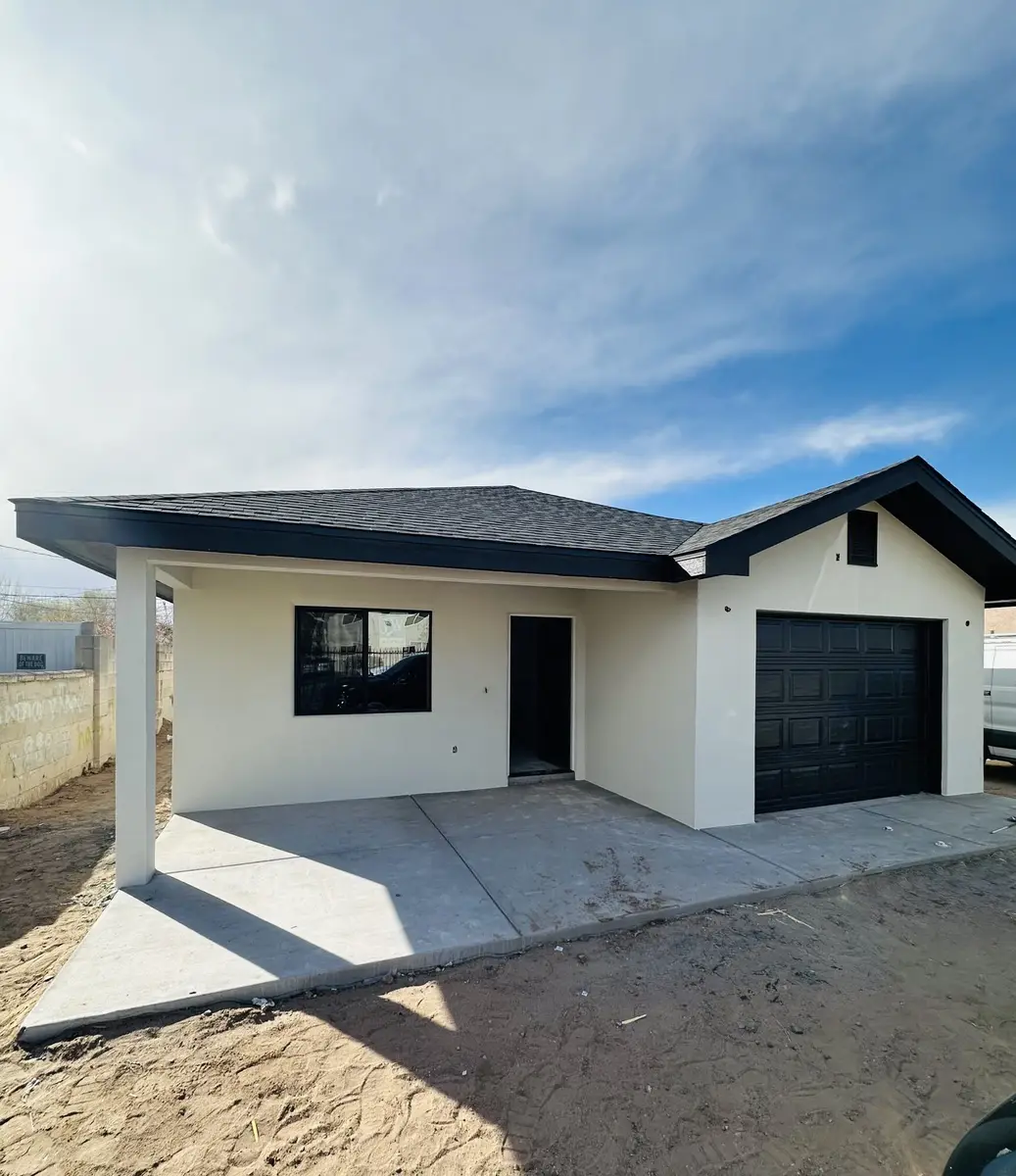 Newly built house finished in white stucco with black window frames, a black garage door and fresh concrete.