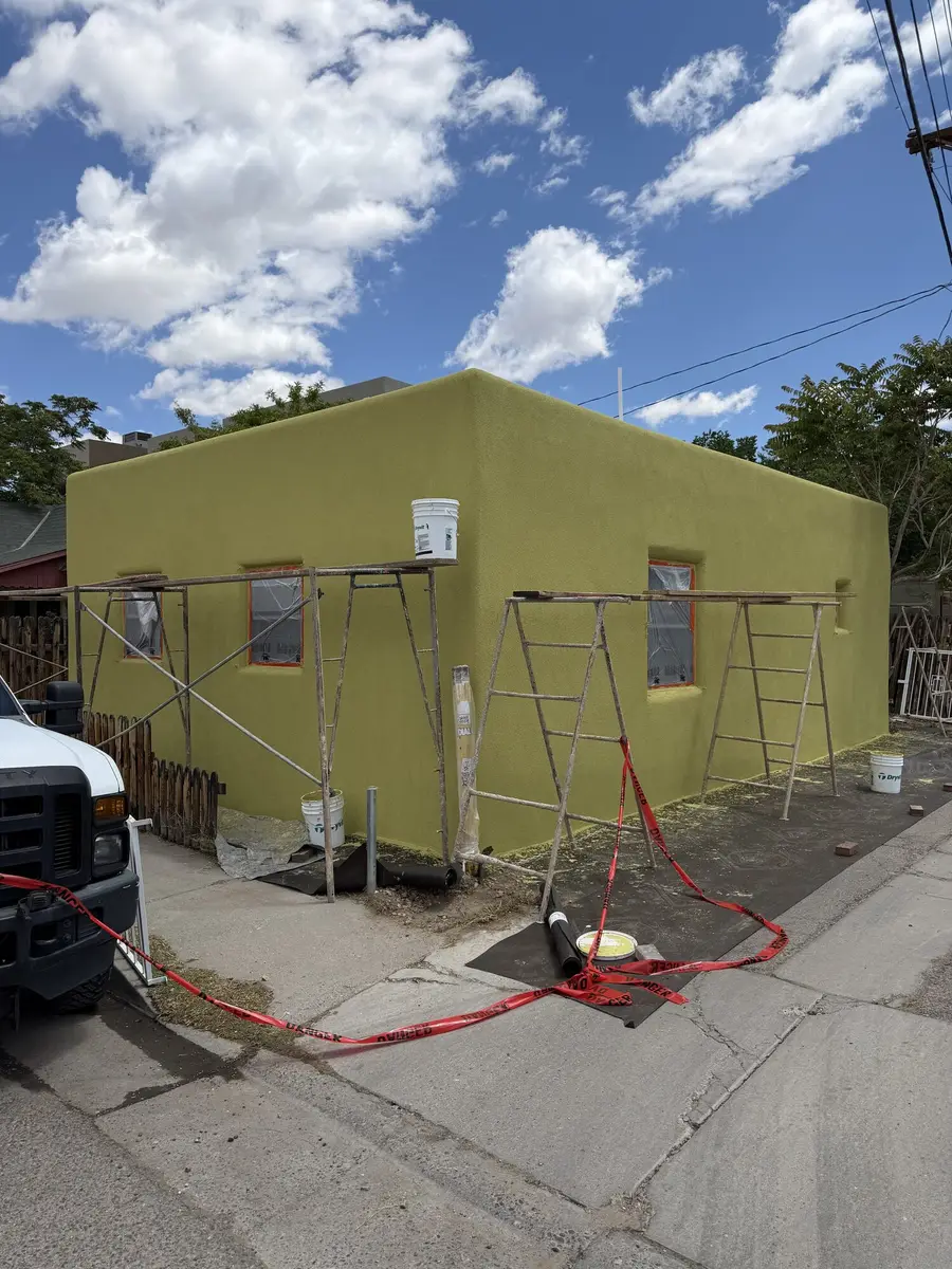 Small house in a fresh yellow green stucco finish with scaffolding planks still standing against the walls.